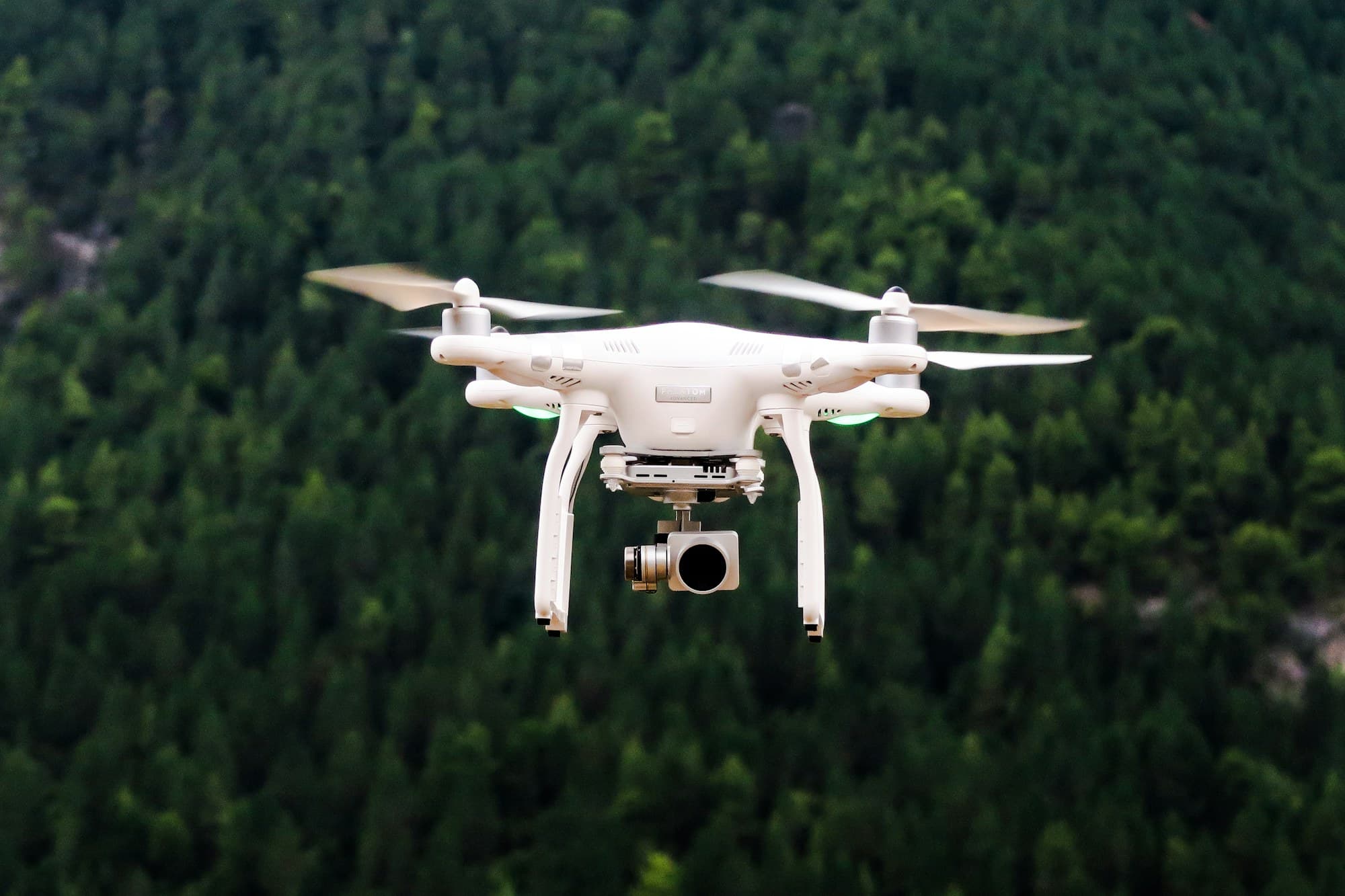Drone blanc en vol stationnaire au-dessus d'une forêt